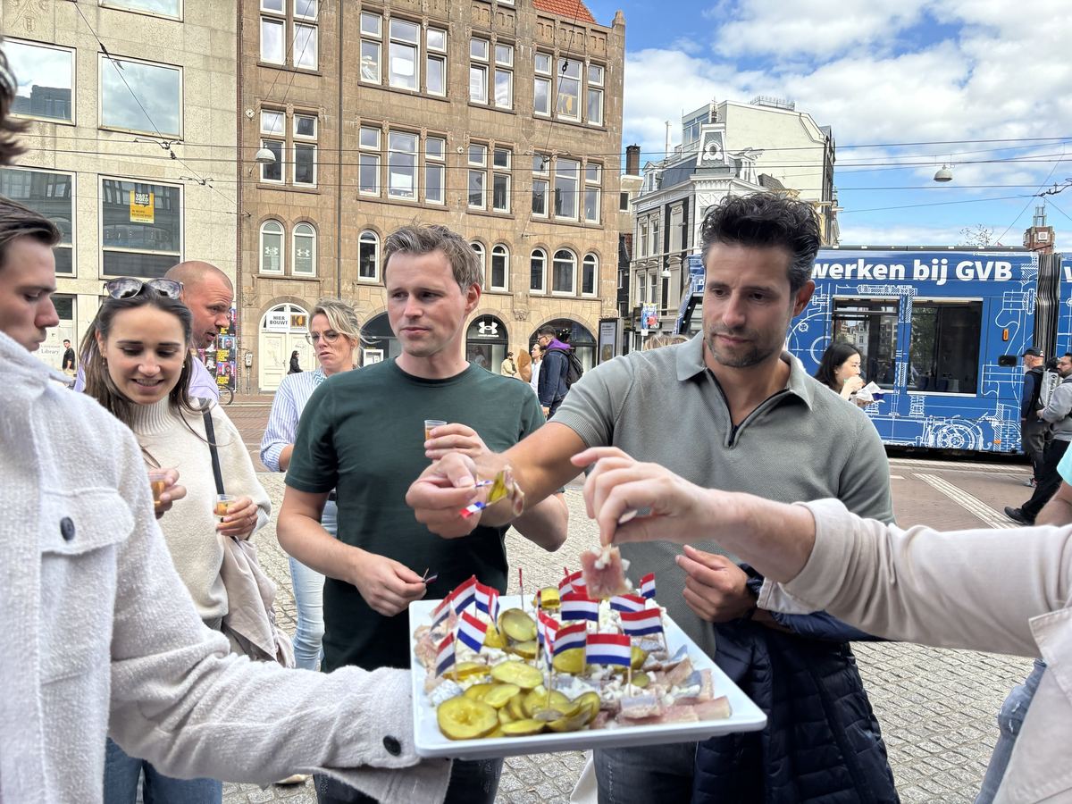 Tour guests tasting herring with pickles and little Dutch flags on a square
